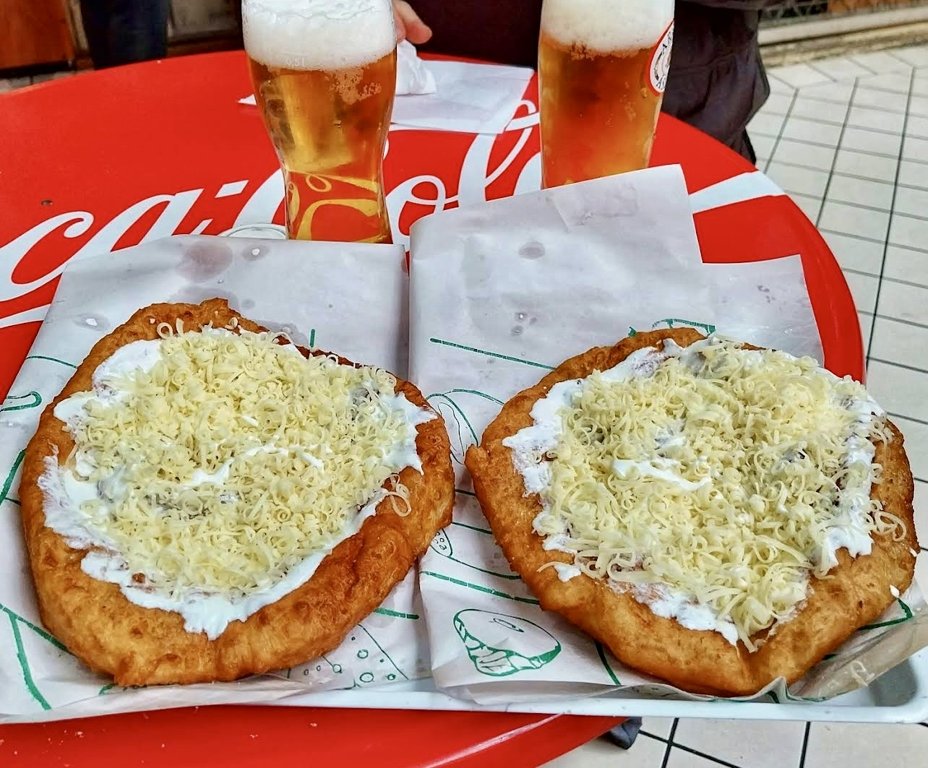 Lángos Centrum’da kırmızı masa üzerinde iki peynirli ve ekşi kremalı lángos