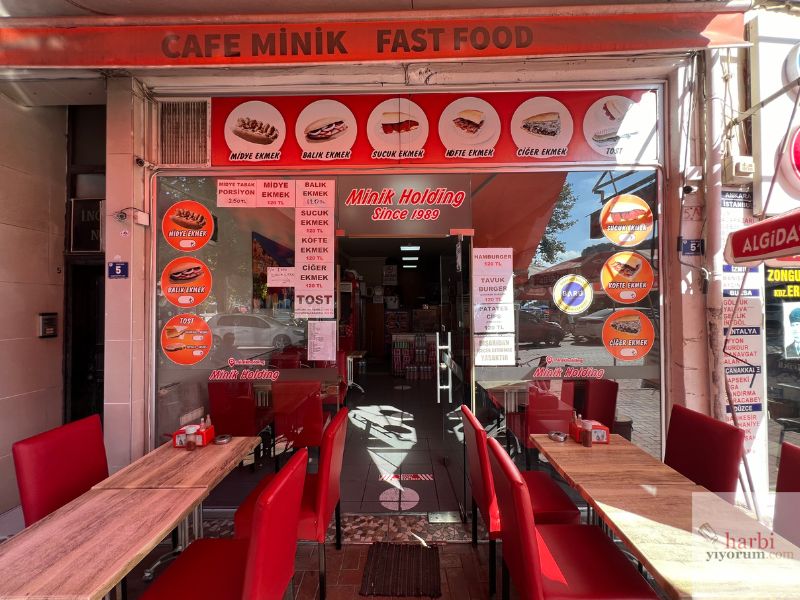 Amasra’da yer alan Minik Holding Cafe Fast Food’un dış cephesi. 1989'dan beri hizmet veren bu mekân, midye ekmek, balık ekmek, köfte ekmek gibi lezzetleriyle dikkat çekiyor. Kırmızı ağırlıklı oturma alanları ve sade, samimi bir atmosfer sunuyor.