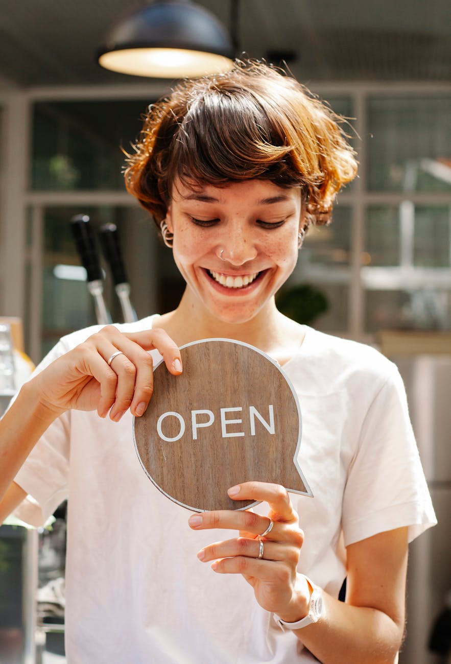 through window of cheerful woman with sign open in cafe